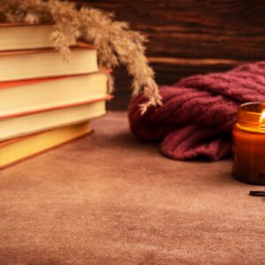 Cozy autumn still life with stack of books and glowing candle on dark brown table with copy space