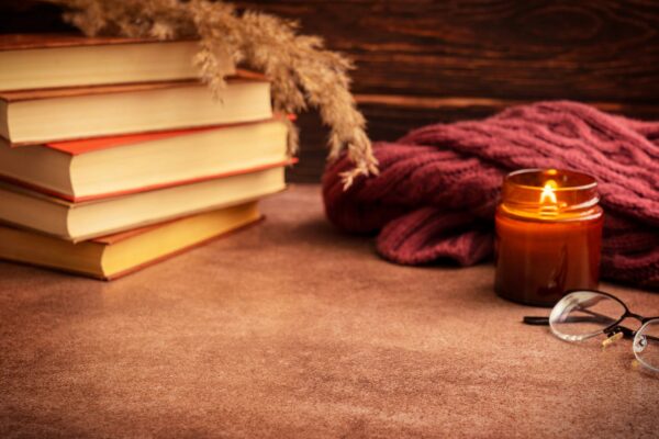 Cozy autumn still life with stack of books and glowing candle on dark brown table with copy space